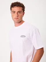 Remera blanca de manga corta y corte holgado de la marca Rusty, con estampado gráfico en la espalda con el logo de la marca en tonos grises.