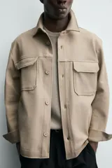 Sobrecamisa relaxed fit color beige con tejido elástico, cuello solapa, manga larga con puños abotonados, bolsillos de plastrón con solapa en el pecho, bolsillos laterales de vivo en la cadera y cierre frontal de botones.