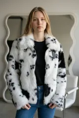 Abrigo corto de piel sintética con estampado de manchas blancas y negras, tipo dálmata. Presenta cierre frontal con cremallera metálica, cuello solapa y detalles de tiras con hebillas en la parte superior.