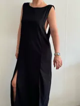 Vestido largo negro de tejido texturizado, sin mangas y con escote bote. Presenta dos tajos laterales altos.