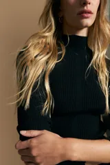 Polera de tejido acanalado con cuello alto, corte ajustado al cuerpo y mangas tres cuartos con terminaciones onduladas en los puños.