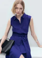 Vestido midi de corte evasé y diseño sin mangas, confeccionado en tejido texturizado color azul. Presenta cuello camisero, cierre frontal con botones, bolsillo de parche en el pecho y un lazo ajustable en la cintura.