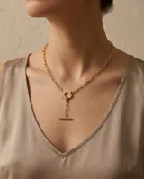 Collar de acero con baño de oro, compuesto por una cadena de eslabones cuadrados, un dije central en forma de flor y un cierre tipo barra en T.