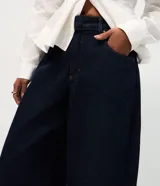 Pantalón de jean azul oscuro con corte barrel, tiro alto y diseño de piernas amplias con terminación afinada. Cuenta con cintura con pasadores, cierre frontal con botón y bolsillos funcionales.