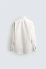 Camisa de corte relajado color celeste, confeccionada en mezcla de algodón y seda. Presenta cuello solapa, cierre frontal de botones, manga larga con puños abotonados y dos bolsillos de plastrón con solapa en el pecho.