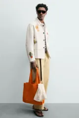 Bolso tipo shopper de color naranja con acabado trenzado y diseño estructurado. Cuenta con compartimento principal y dos asas cortas de mano.