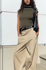 Top de tejido de punto acanalado color verde militar, con cuello alto tipo tortuga y mangas sisa. Presenta un bajo asimétrico con aberturas laterales.