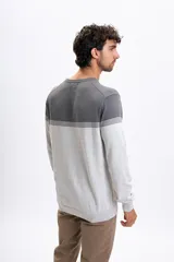 Buzo de punto con diseño de bloques de color en tonos gris oscuro y gris claro, separado por finas franjas horizontales. Presenta cuello redondo y puños acanalados.
