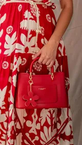 Cartera de mano color bordó, con correa larga desmontable y charm colgante de flor.