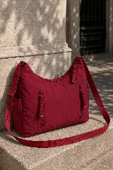 Cartera hobo gris de tela suave y liviana, con bolsillos frontales con cierre y tiradores trenzados, correa ajustable y compartimento principal con cierre.