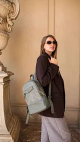 Mochila de diseño minimalista en color verde oliva, confeccionada en símil cuero. Presenta un bolsillo frontal con solapa y cierre, apertura superior con cierre y correas regulables para la espalda, además de un asa de mano superior.