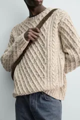 Jersey de punto con diseño de trenzas diagonales, confeccionado en lana con efecto moteado. Presenta cuello redondo, manga larga y terminaciones en rib.