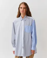 Camisa de corte recto y ligeramente oversize, confeccionada en algodón orgánico. Presenta un diseño a rayas con paneles en contraste de tonos azules y blancos, cuello clásico, cierre frontal de botones y un bolsillo en el pecho.