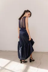 Pollera midi de tafeta color negro, con diseño asimétrico de corte mullet (más corta adelante y larga atrás), tiro alto y detalle de volado fruncido en el ruedo.