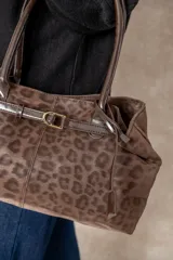 Cartera tipo shopper color chocolate con estampado animal print, confeccionada en material tipo gamuza, con asas cortas rígidas y detalle de cinturón decorativo con hebilla en el frente.