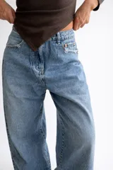 Pantalón de jean estilo palazzo en tono celeste medio, con corte amplio y tiro medio. Presenta sutiles detalles de roturas en los bolsillos y en el ruedo deshilachado.