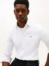 Camisa blanca de corte regular de Tommy Hilfiger, confeccionada en puro algodón regenerativo con diseño de raya diplomática y sutil textura diagonal. Presenta cuello camisero, cierre frontal de botones y el logo de la marca bordado en el pecho.
