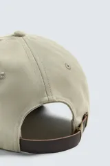 Gorra de seis paneles de algodón en color beige con visera marrón contrastante. Cuenta con un diseño bordado en marrón en el frente con texto alusivo.