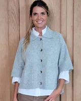 Cardigan de lana lambswool color gris melange, con cuello camisero, cierre frontal de botones y mangas cortas con terminación acanalada. Presenta dos bolsillos frontales tipo parche.