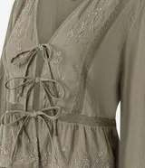 Blusa tipo bata de algodón color verde oliva, con escote en V, cierre frontal mediante lazos, mangas largas y detalles de bordados florales y encaje en el frente.