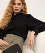 Camisa de crepé color blanco, con cuello inglés, manga larga abullonada con puños abotonados y cierre frontal oculto con botón diferenciado en el cuello.