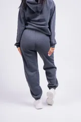 Pantalón de jogging gris oscuro, de corte holgado con cintura elástica y puños ajustados en los tobillos. Presenta bolsillos laterales y un pequeño logo bordado en la pierna izquierda.