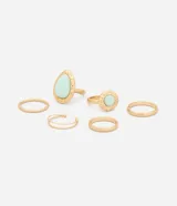 Set de seis anillos de metal dorado con diseños variados, incluyendo modelos lisos, texturizados, martillados y con piedras naturales en tonos verde agua. Incluye un anillo doble articulado y una pieza con aro ajustable.
