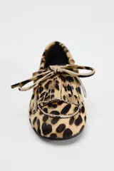 Mocasín plano de piel con pelo con estampado animal print, detalle de flecos y lazo en la parte delantera, pespuntes en contraste y punta redonda.