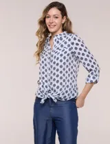 Camisa de gasa blanca con estampado de lunares en tonos azules, cuello con solapa, cierre frontal de botones, bolsillo aplicado en el pecho y detalle de nudo en el dobladillo inferior. Cuenta con mangas largas regulables.