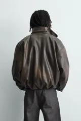 Cazadora de corte relajado confeccionada en tejido efecto piel con acabado lavado. Presenta cuello subido, cierre frontal de cremallera, mangas largas con puños elásticos y ruedo elástico. Incluye bolsillos laterales y un bolsillo interior.