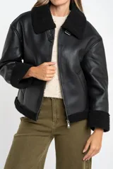 Campera tipo gamulán de cuero sintético negro con interior y detalles de cuello y puños en corderito negro. Presenta cierre frontal y diseño oversize.