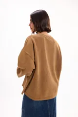Buzo oversize color marrón con cuello redondo, mangas largas amplias y puños acanalados. Presenta letras en relieve con efecto desflecado en el frente y ruedo con terminación desflecada.
