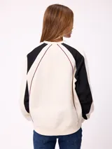 Buzo de cuello redondo con diseño color block, cuerpo en tono crema y mangas negras con detalles de costuras en color bordó. Presenta logo de la marca estampado en el centro del pecho y corte holgado.