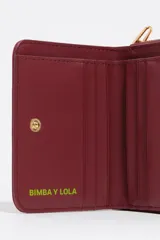 Billetera compacta de nylon color beige, con cierre de cremallera perimetral y tirador decorativo con cordón. Presenta el logo metálico de la marca en el frente.