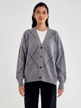 Cardigan de punto gris, corte oversize, con escote en V y botones frontales. Presenta un patrón de rombos formado por líneas de micro lentejuelas negras.