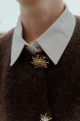 Chaleco de punto en color marrón oscuro, con cuello redondo y cierre frontal mediante botones metálicos decorativos con forma de sol.