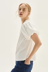 Blusa blanca de calce recto con cuerpo de jersey y mangas cortas tipo globo en popelina. Presenta cuello redondo y detalle de bordado decorativo en la espalda.