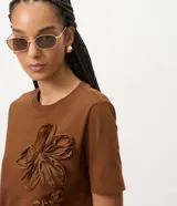 Remera de algodón marrón de manga corta y cuello redondo, con apliques tridimensionales de flores en relieve en el frente.