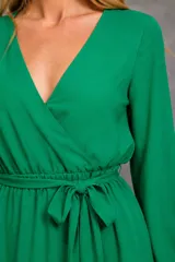 Vestido largo verde con escote cruzado en V, mangas largas amplias con puños elásticos y lazo ajustable en la cintura.
