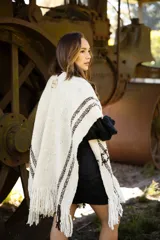 Ruana artesanal de lana merino en color crudo con detalles de líneas horizontales en color marrón chocolate y terminación con flecos en el ruedo.