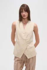 Chaleco color beige claro, sin mangas, con escote en V profundo y cierre frontal asimétrico con botones.