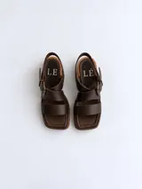 Sandalias de cuero negro con textura croco, punta cuadrada y taco bloque de altura media. Cuenta con tiras cruzadas en el empeine y una hebilla metálica grande decorativa.