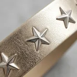 Cinto dorado de símil cuero con detalles de tachuelas en los bordes y apliques de estrellas metálicas, con hebilla plateada clásica.