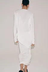 Jersey de punto liso blanco, con cuello redondo y mangas largas. Presenta un diseño de bajo asimétrico pronunciado.