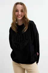 Buzo negro con efecto lavado, cuello redondo y manga larga. Presenta un diseño estampado en relieve con forma de corazón y la inscripción "Good Mood" en el centro.