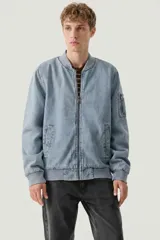Campera tipo bomber confeccionada en denim con efecto lavado. Presenta cierre frontal, cuello, puños y ruedo en tejido rib, además de un bolsillo con cierre en la manga izquierda.