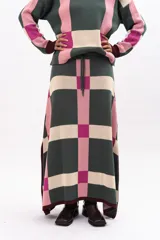 Pollera midi de tejido de punto con diseño geométrico de cuadros en tonos verde, rosa y beige. Presenta cintura elástica con cordón de ajuste y aberturas laterales en el ruedo.