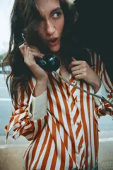 Camisa de manga larga con estampado de rayas verticales en color naranja y crema. Presenta cuello solapa, cierre frontal con botones dorados y puños anchos en color crema con detalle de lazos ajustables.