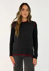 Chaleco de punto gris oscuro con detalles de borde en color bordó en el cuello, sisas y ruedo. Presenta un diseño tejido con terminaciones acanaladas y un pequeño aplique metálico decorativo en la parte inferior.