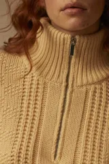 Sweater tejido color crema con cuello alto y cierre metálico frontal parcial.